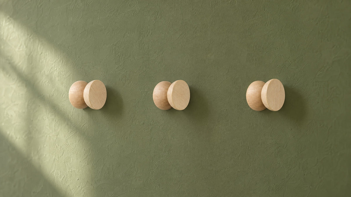 Three round geometric beech wood hooks in a row on an olive-green plaster wall in soft morning light