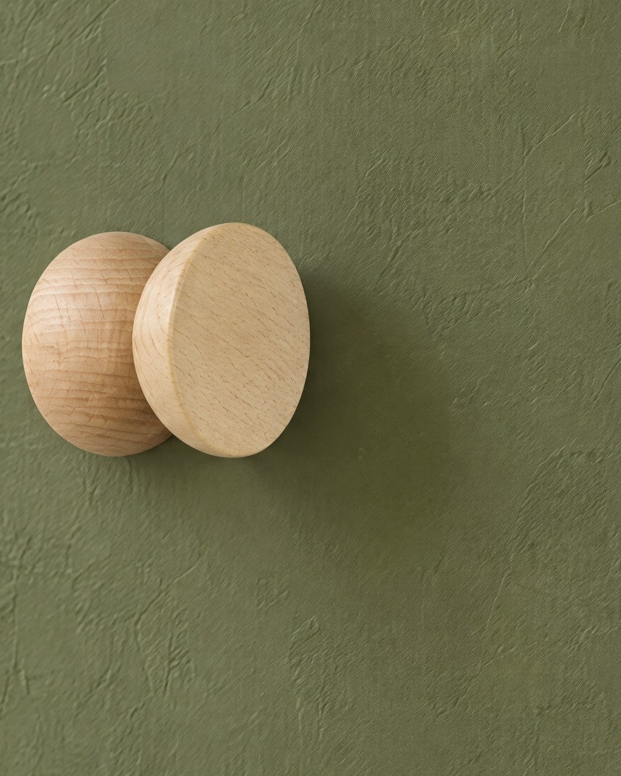 One beech wood hook from the side, two rounded halves joined at a narrow waist, on an olive-green wall