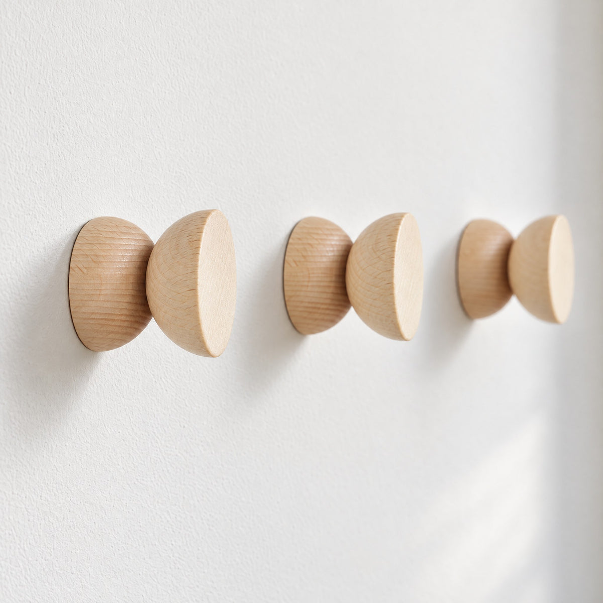Three round beech wood hooks in a row on a white wall, seen from the side