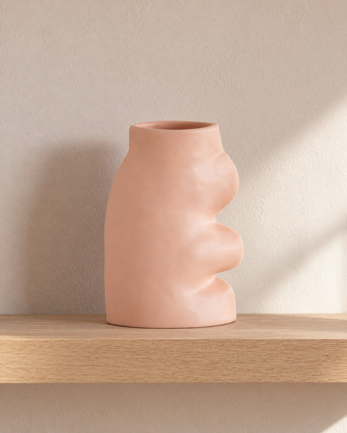 Fluxo large pink ceramic vase, empty, on a light oak wall shelf against a blush plaster wall