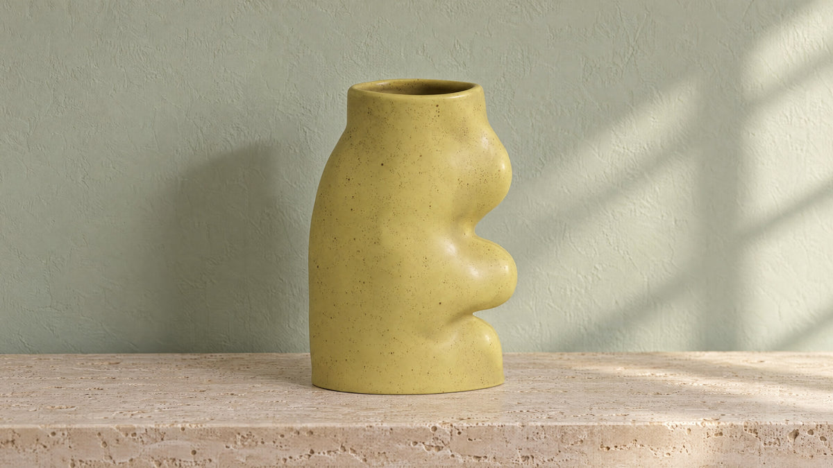 Fluxo large pistachio green ceramic vase, empty, on a travertine console against a pale sage wall in morning light