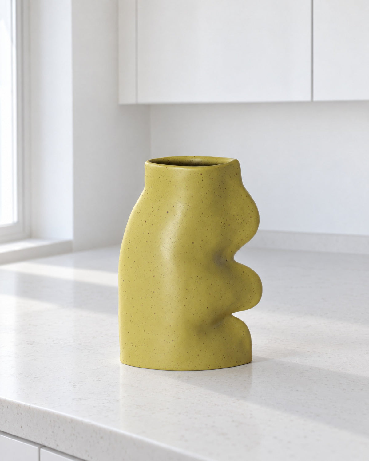 Fluxo large pistachio green ceramic vase, empty, on a white stone kitchen counter in daylight