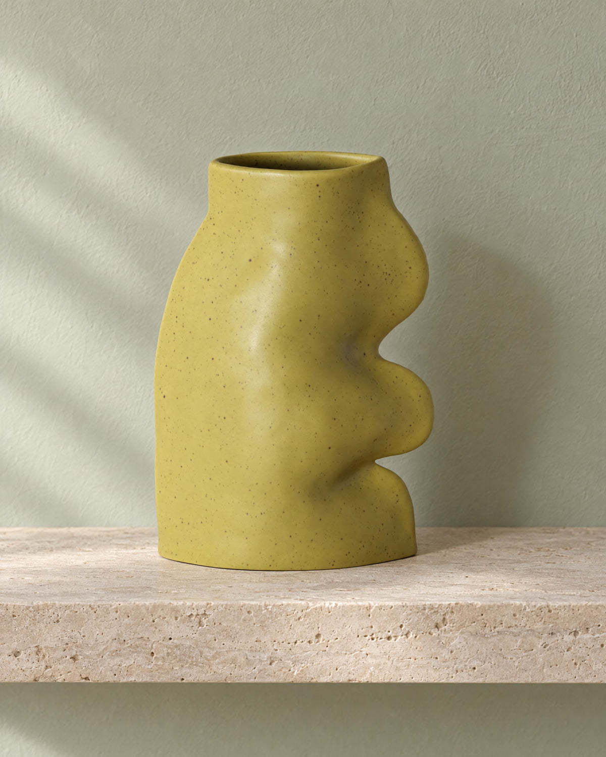 Fluxo large pistachio green ceramic vase, empty, on a travertine wall shelf against a sage plaster wall