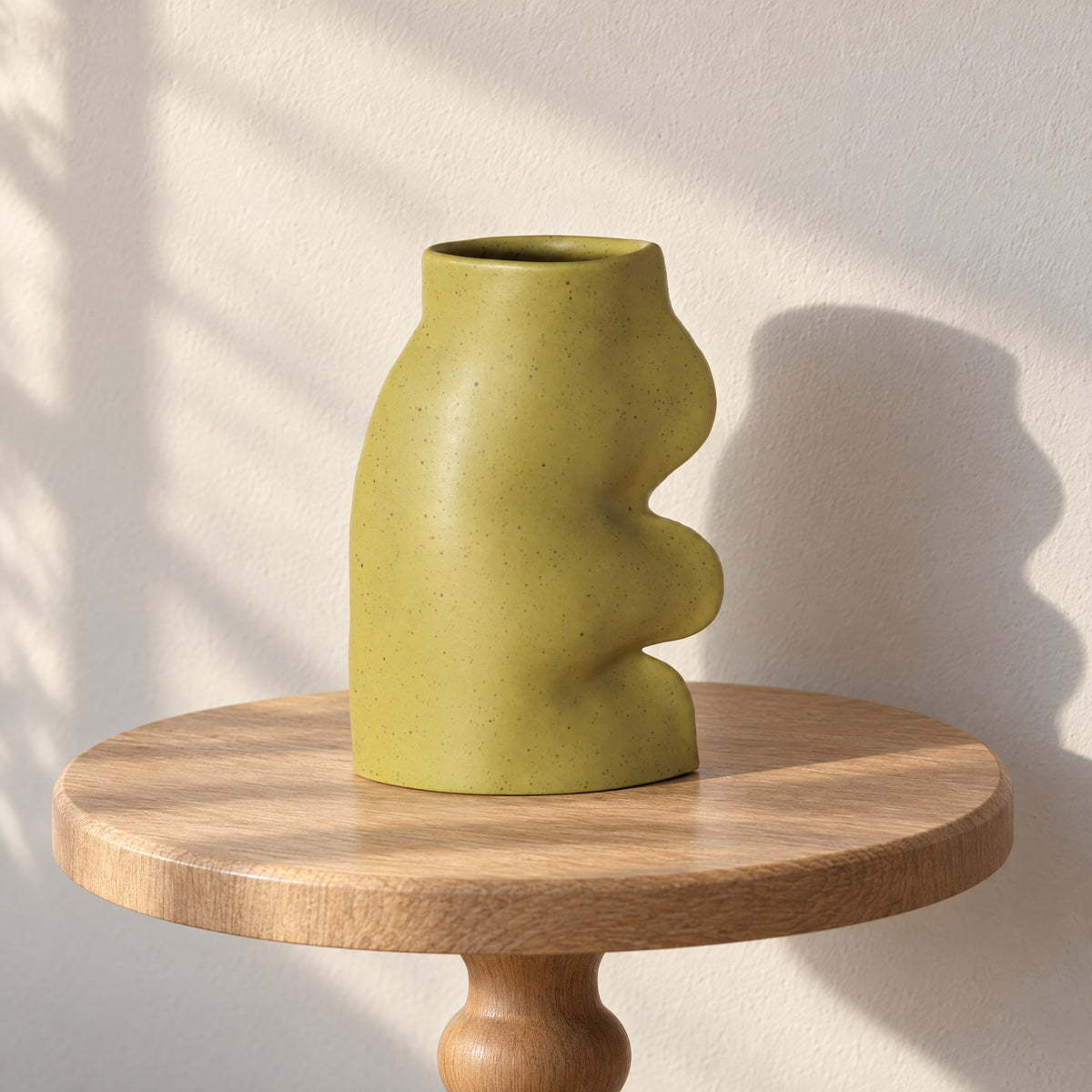 Fluxo large pistachio green ceramic vase, empty, on a round oak side table in afternoon sun