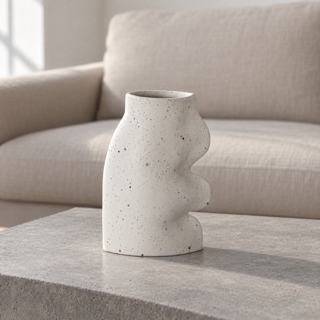 Fluxo large white speckled ceramic vase, empty, on a grey concrete coffee table in front of a linen sofa