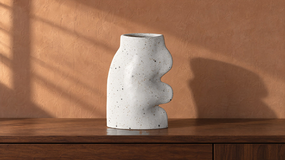 Fluxo large white speckled ceramic vase, empty, on a walnut console against a warm clay wall in raking afternoon sun