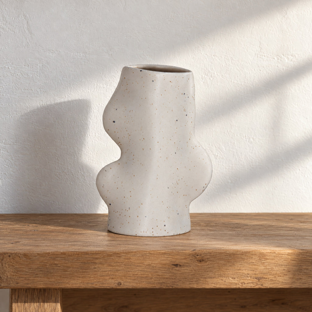 Fluxo medium white speckled ceramic vase, empty, on an oak bench against a white limewash wall in afternoon sun