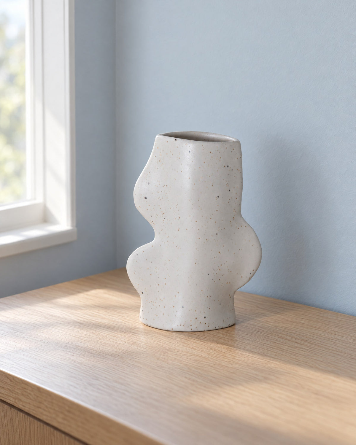 Fluxo medium white speckled ceramic vase, empty, on a light oak desk by a window