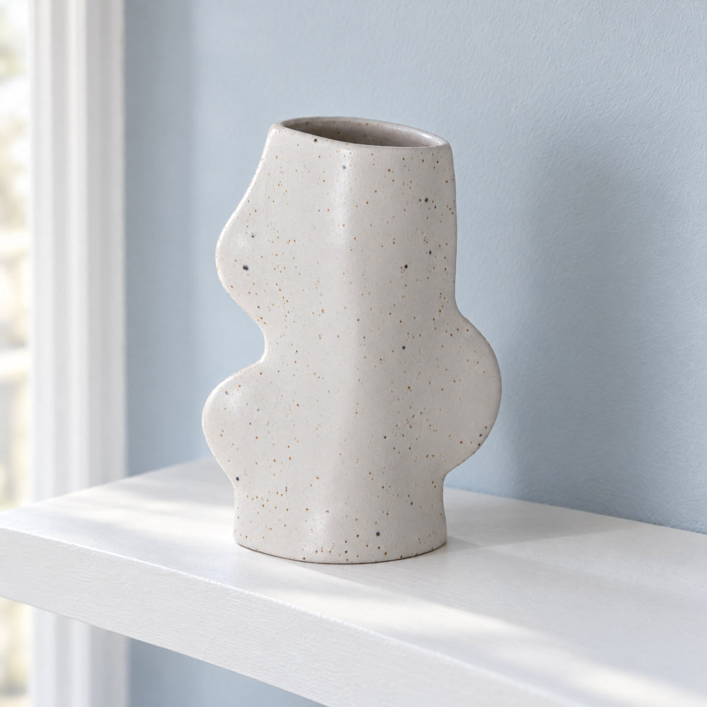 Fluxo medium white speckled ceramic vase, empty, on a white floating shelf in a hallway, seen from slightly above