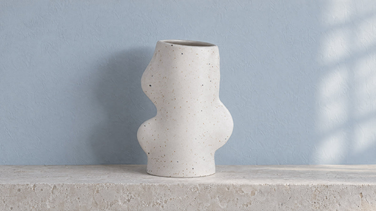 Fluxo medium white speckled ceramic vase, empty, on a pale limestone ledge against a soft blue-grey wall