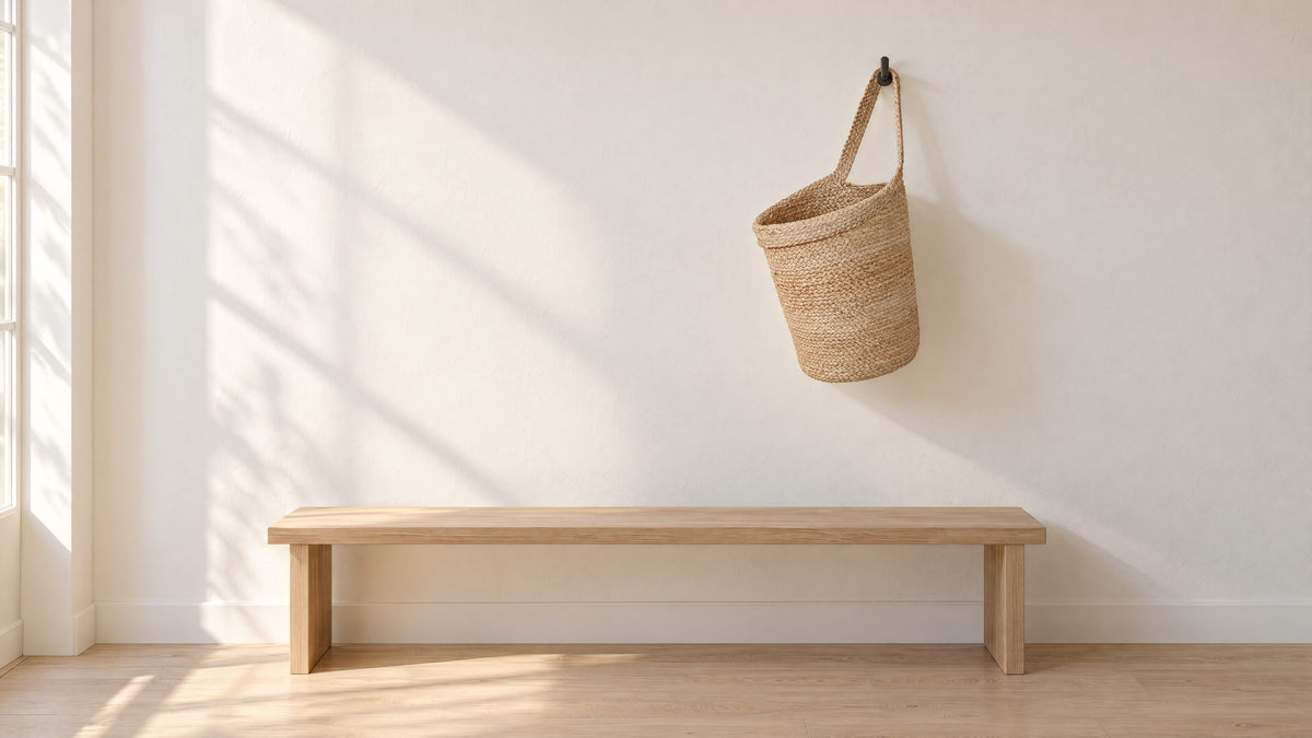 Kata braided jute wall basket hanging by its strap from a black wall hook above a low oak bench (hook not included)