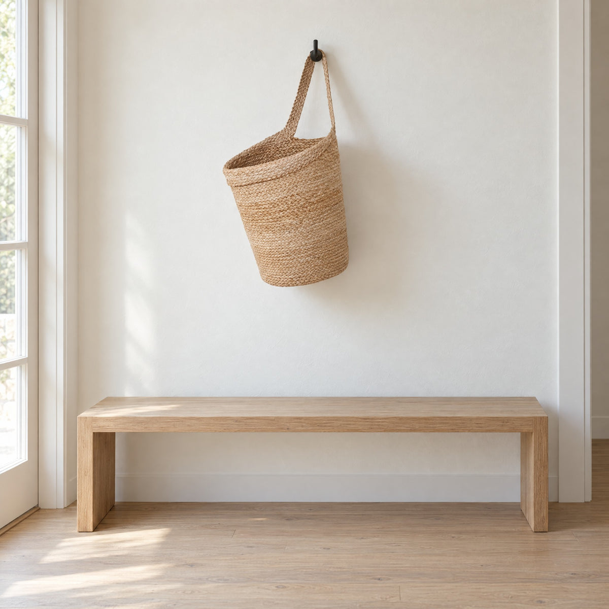 Kata jute basket hanging from a small black wall hook above a low oak bench (hook not included)