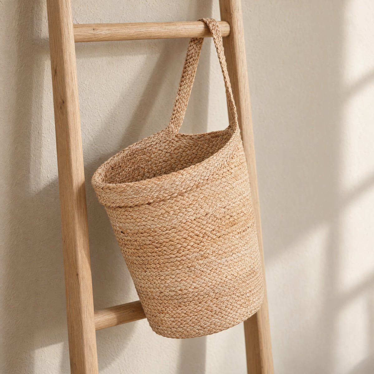 Kata braided jute basket hanging by its strap from the rung of a light oak ladder