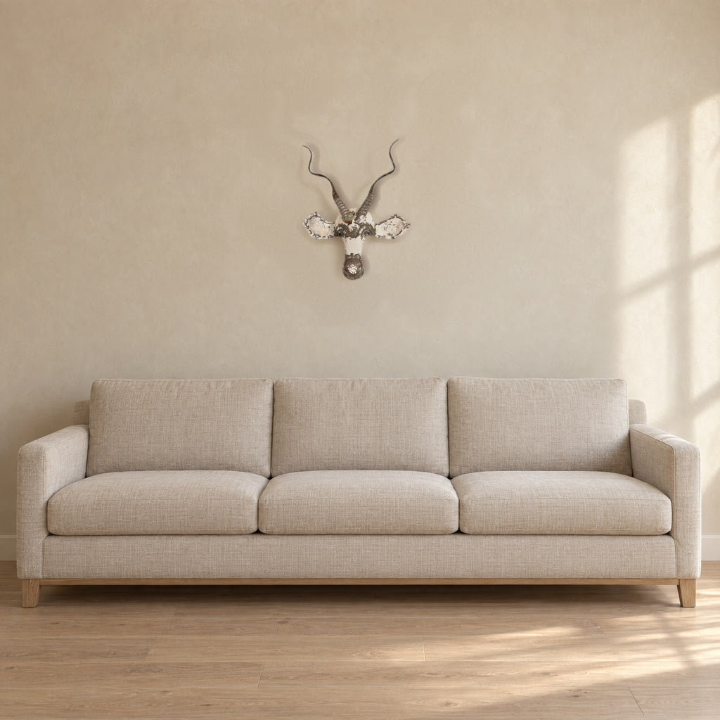 Kudu recycled metal wall mask on a sand-coloured wall above a plain linen sofa