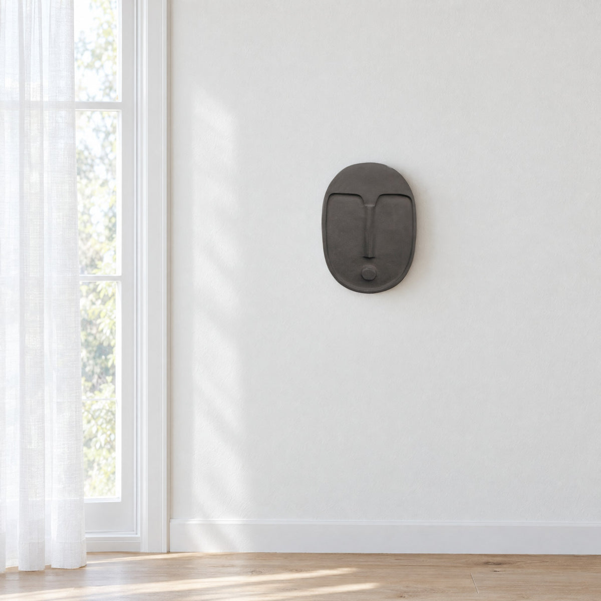 Anthracite grey ceramic wall mask on a white wall beside a tall window with sheer curtains