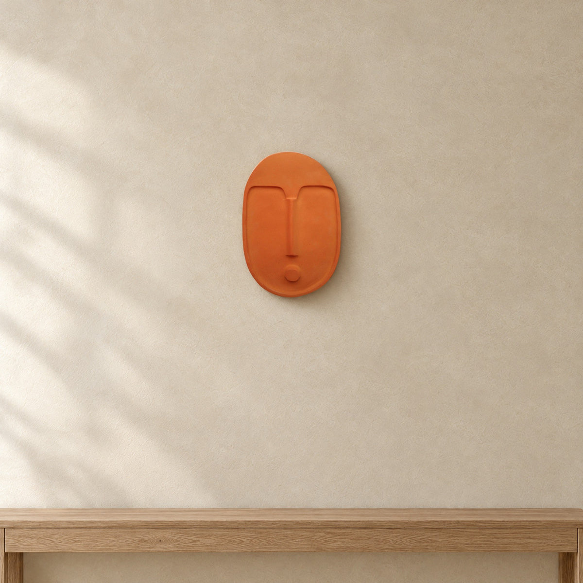 A terracotta ceramic wall mask by 5mm Paper on a limewashed wall above a wooden bench