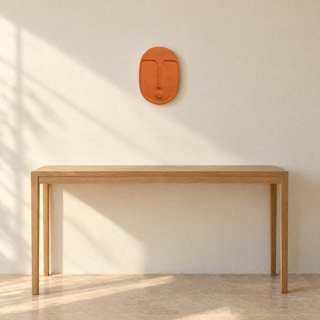 Terracotta ceramic wall mask on a warm off-white plaster wall above a light oak console table