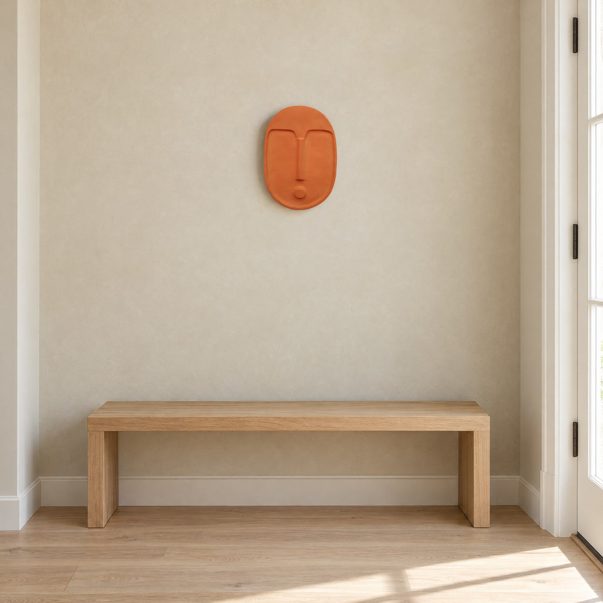 Terracotta ceramic wall mask in a bright hallway above a low oak bench