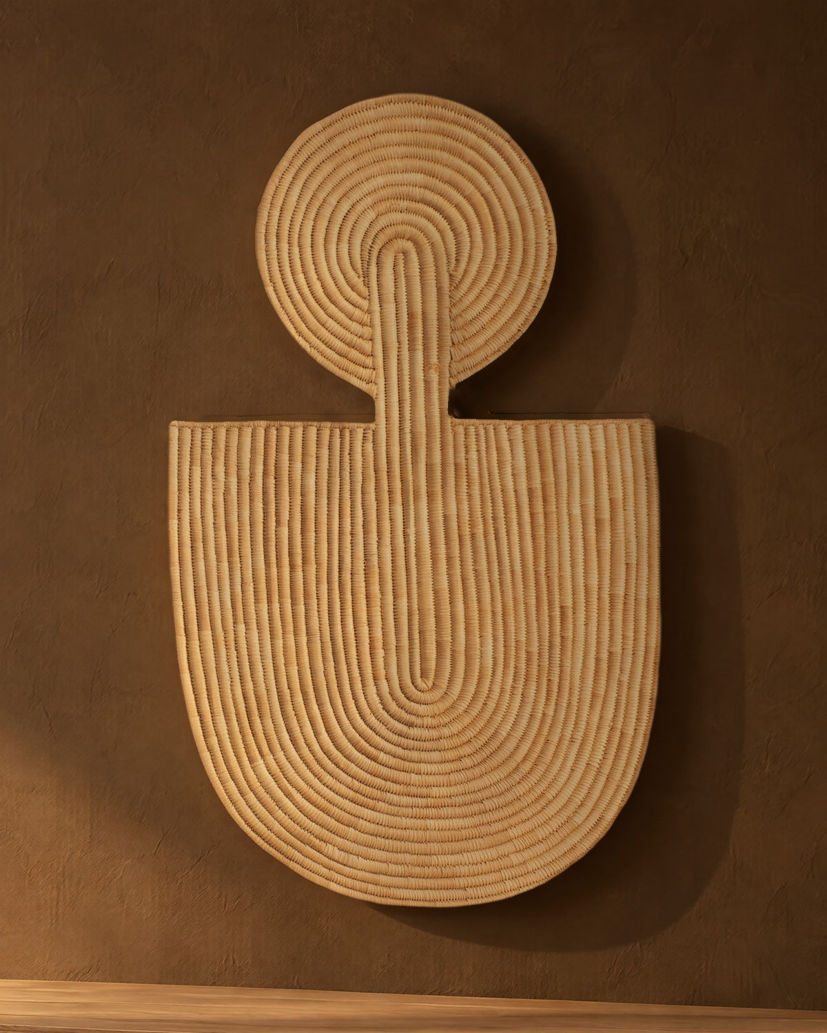Abstract Wall Mask 1 in natural woven fibre on a dark umber plaster wall, in low sun