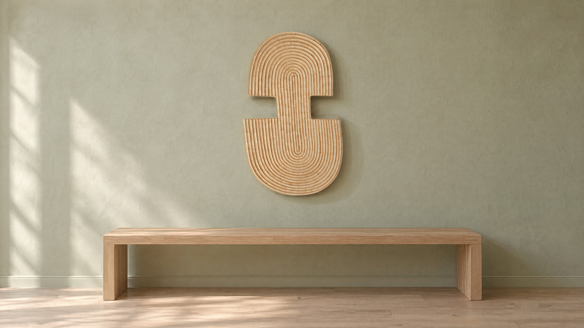 Abstract Wall Mask 2 hung on a pale sage plaster wall above a long low oak bench, in soft window light