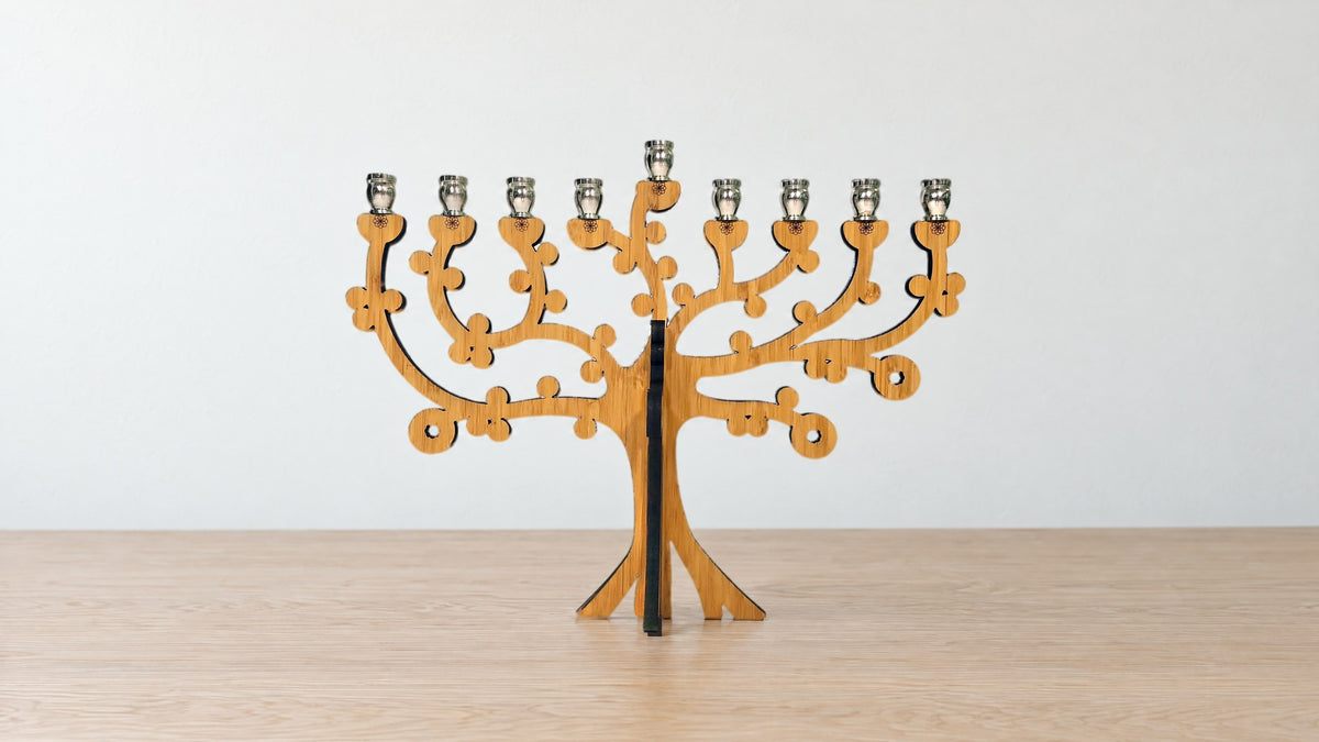 Tree of Life bamboo menorah with nine nickel candle cups on a pale oak table against a plain white wall, no candles
