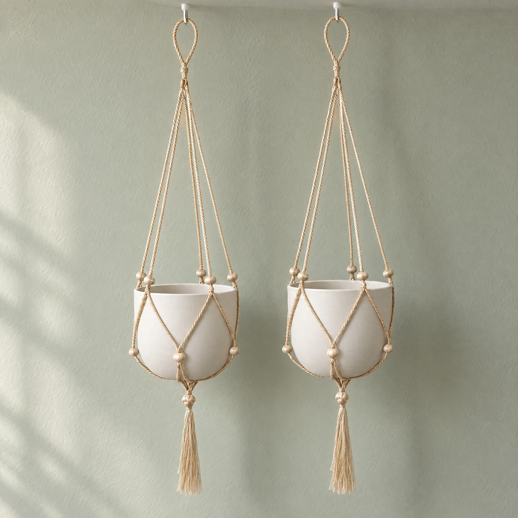 Two Nadu jute macrame plant hangers side by side on a sage-grey wall, shown with plain white pots (pots and hooks not included)