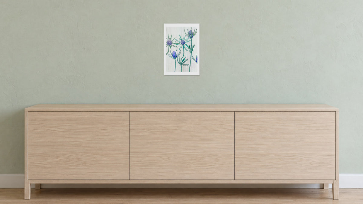 Unframed Purple Thistle on Snow art print, 13 x 19 in size, on a pale sage plaster wall above a white-oak sideboard