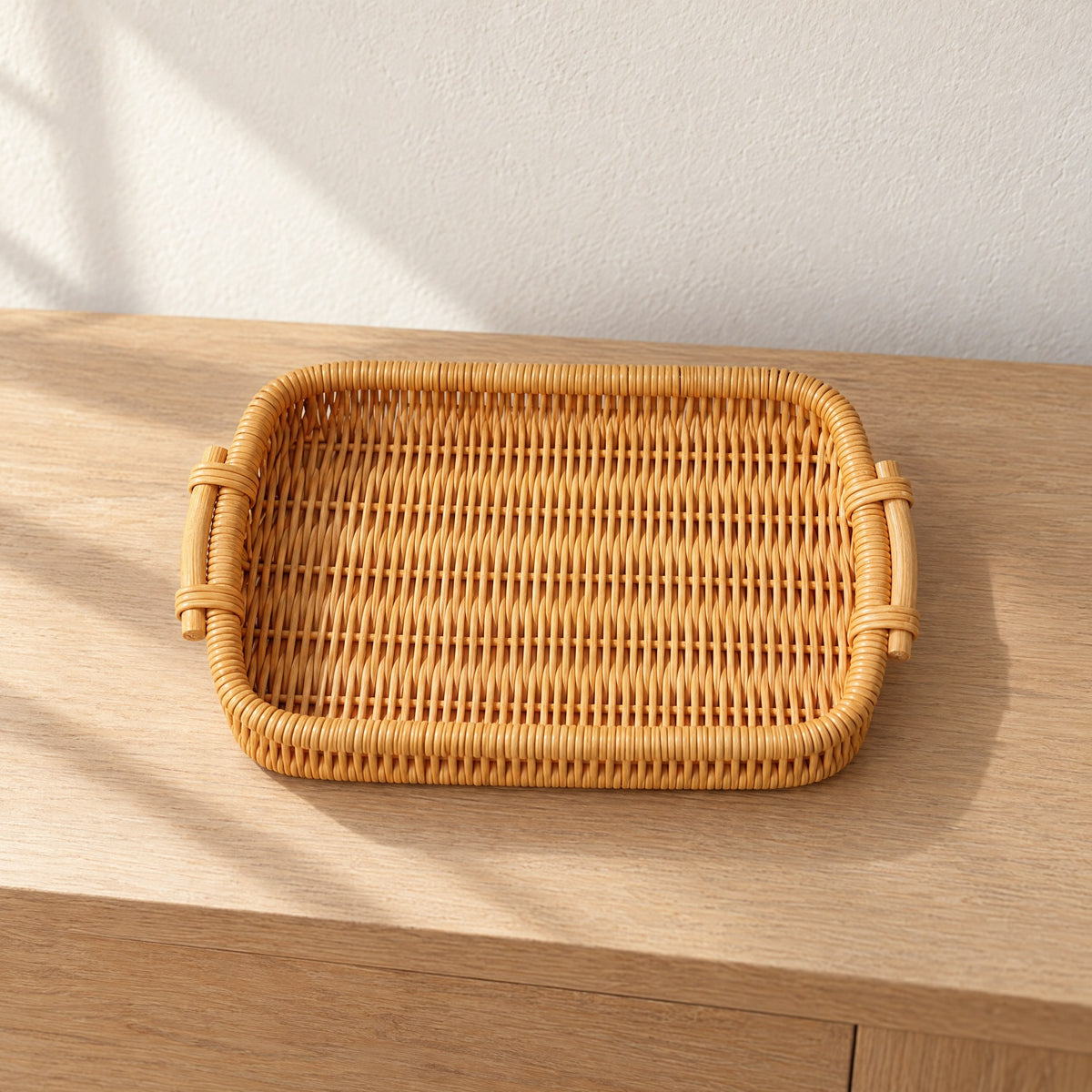 Rectangular honey woven rattan tray with two side handles, empty, on a light oak console