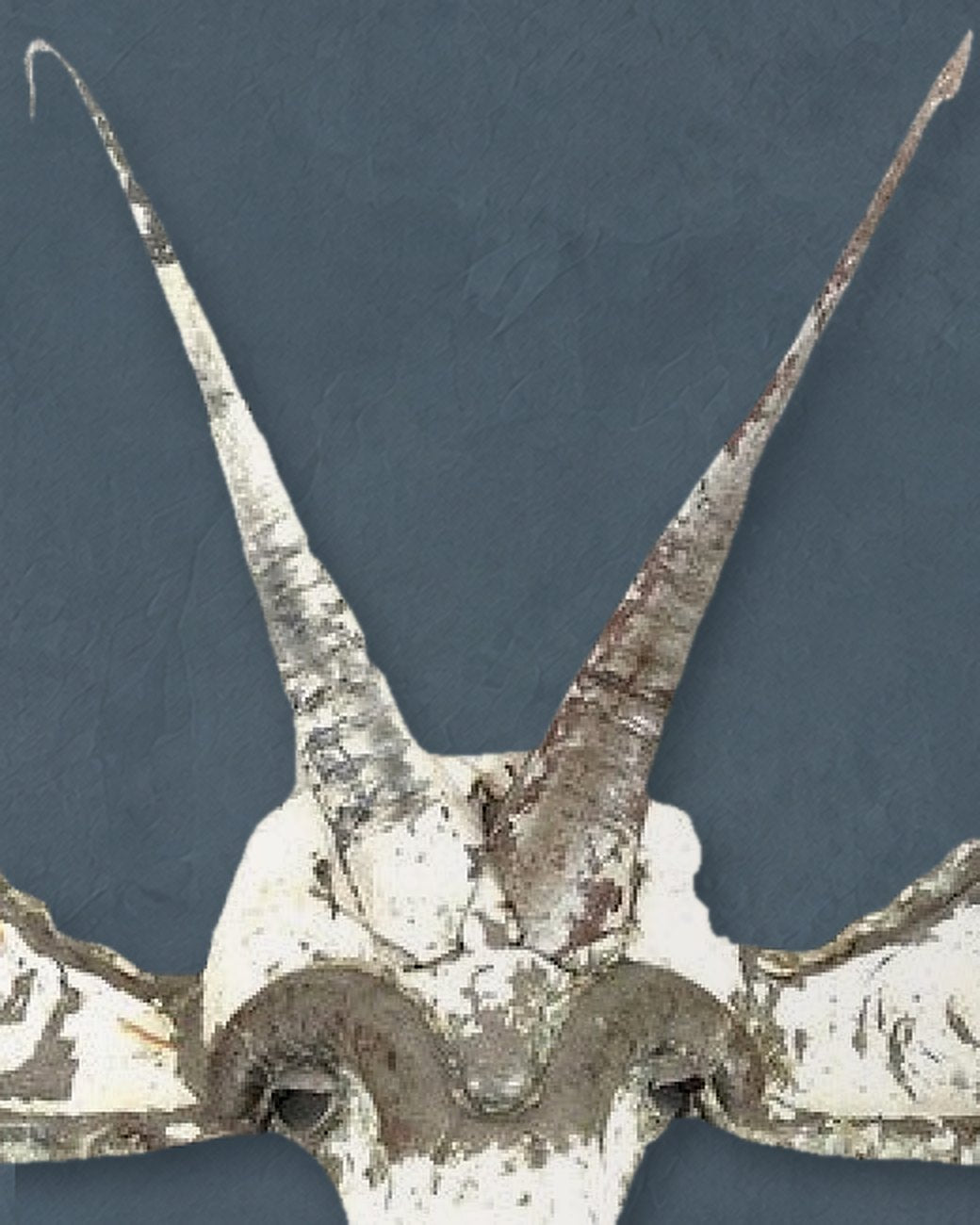 Close-up of the Sable mask’s two long horns rising from the brow, worn white paint over bare metal