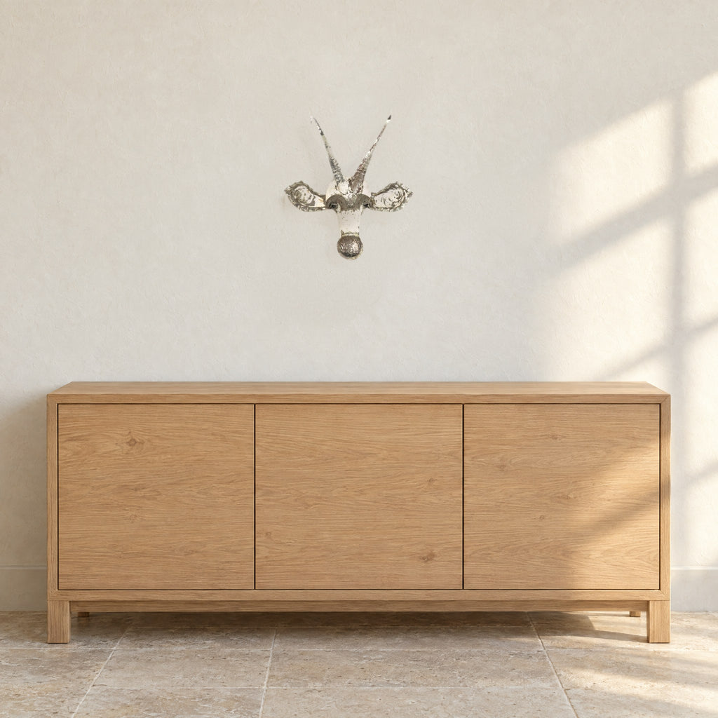 Sable recycled metal wall mask on a warm white wall above a light oak sideboard