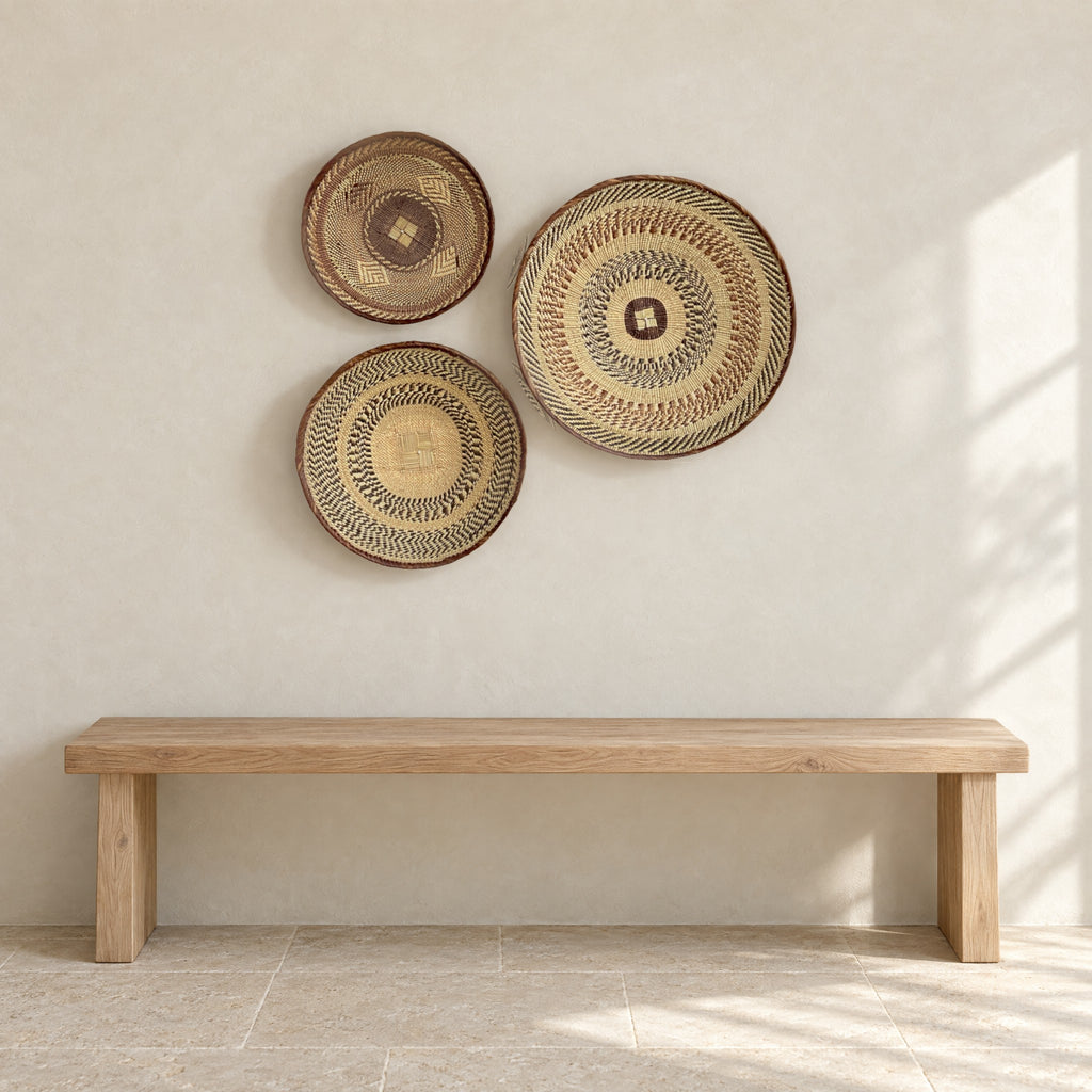 Set of three Tonga baskets hung on a pale limewash wall above a low oak bench