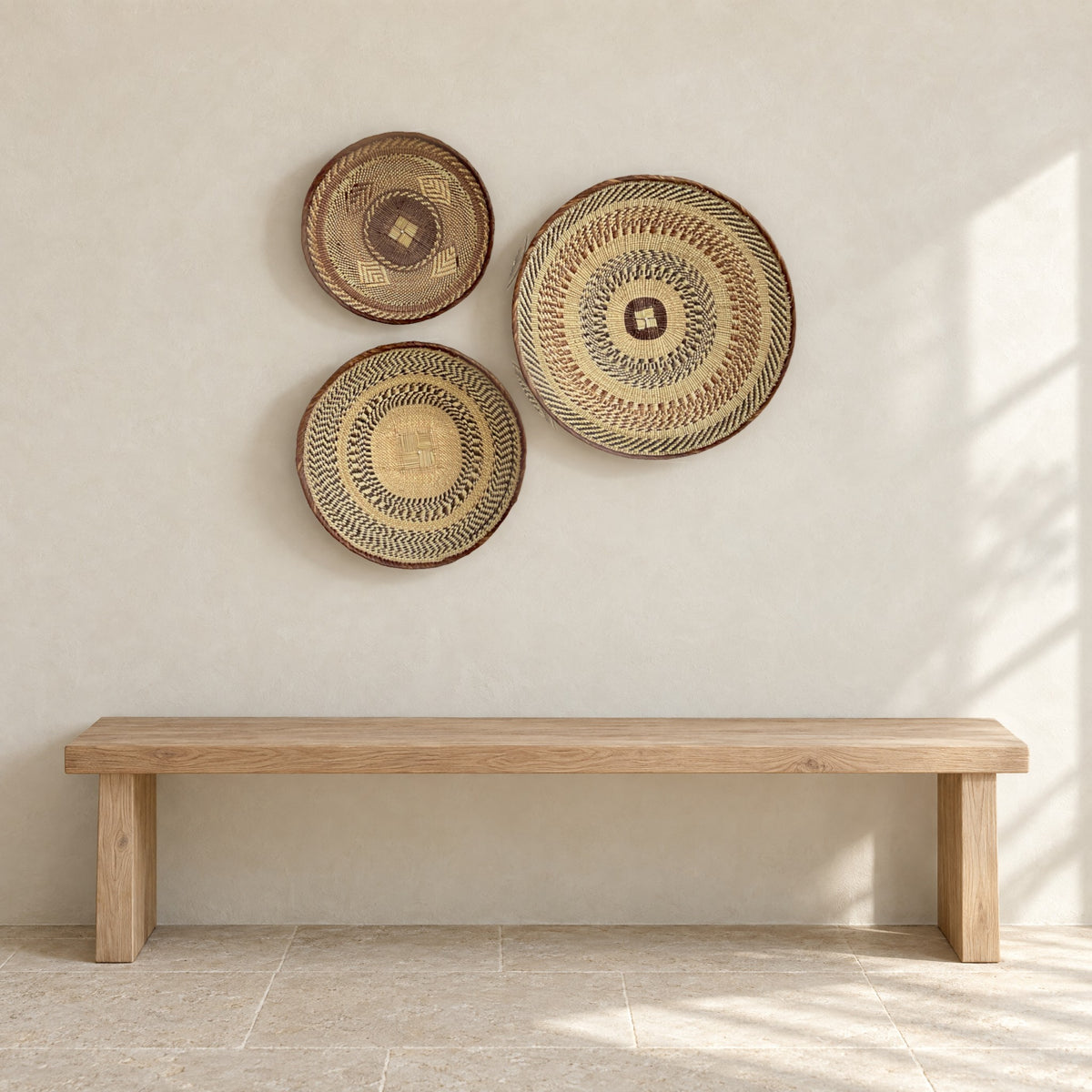 Set of three Tonga baskets hung on a pale limewash wall above a low oak bench