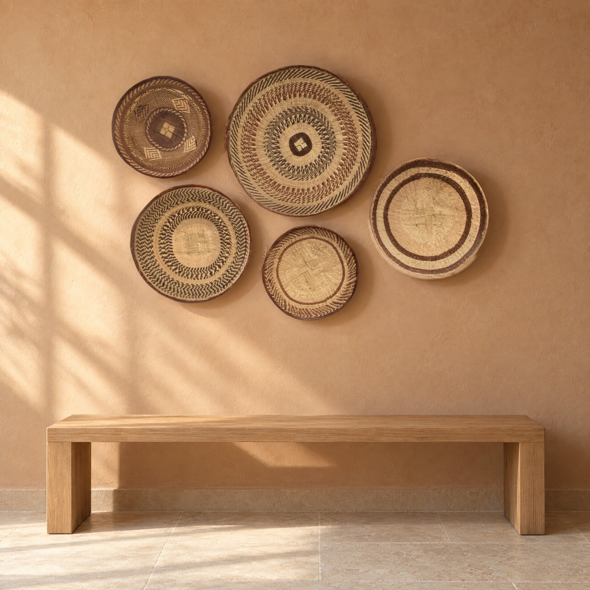 Five Tonga baskets hung on a warm terracotta-beige plaster wall above a low oak bench