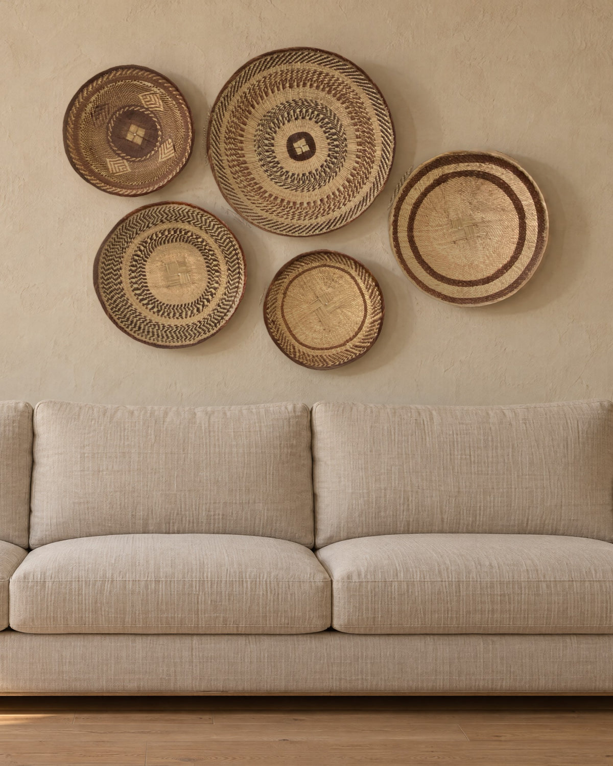 Five Tonga baskets hung above a plain linen sofa on a warm sand plaster wall