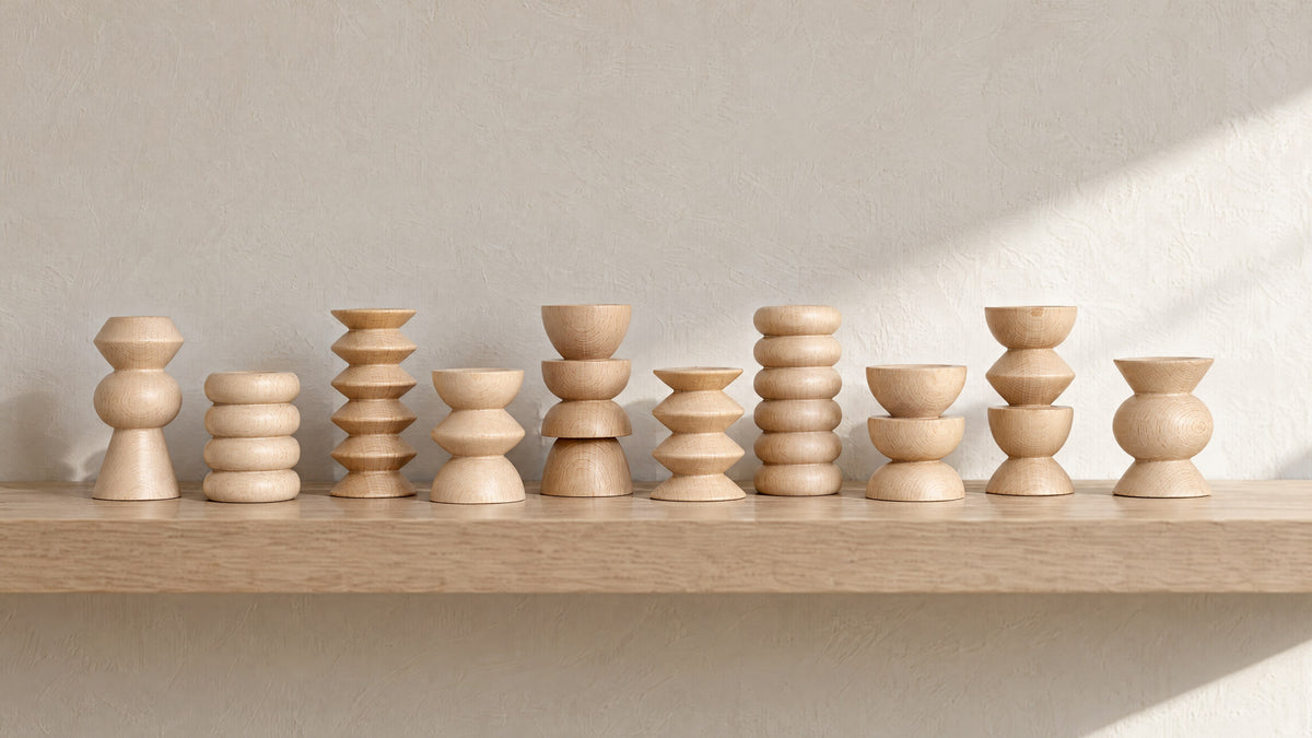 Ten turned beech Totem picture stands in a row on a pale oak wall shelf against an oatmeal plaster wall